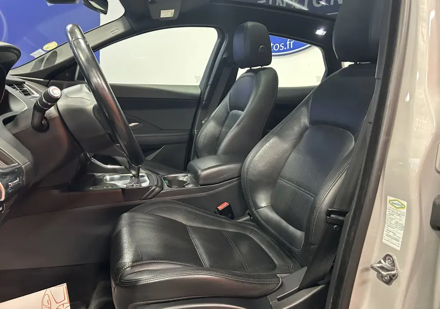 Vue intérieure côté conducteur du Jaguar E-PACE beige 2018, sièges cuir noirs et toit panoramique visible.