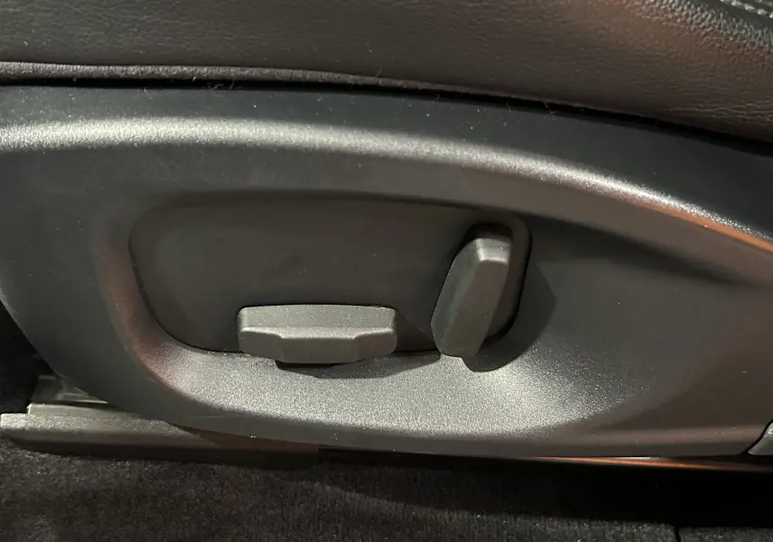 Gros plan sur les commandes électriques de réglage du siège en cuir noir du Jaguar E-PACE beige.