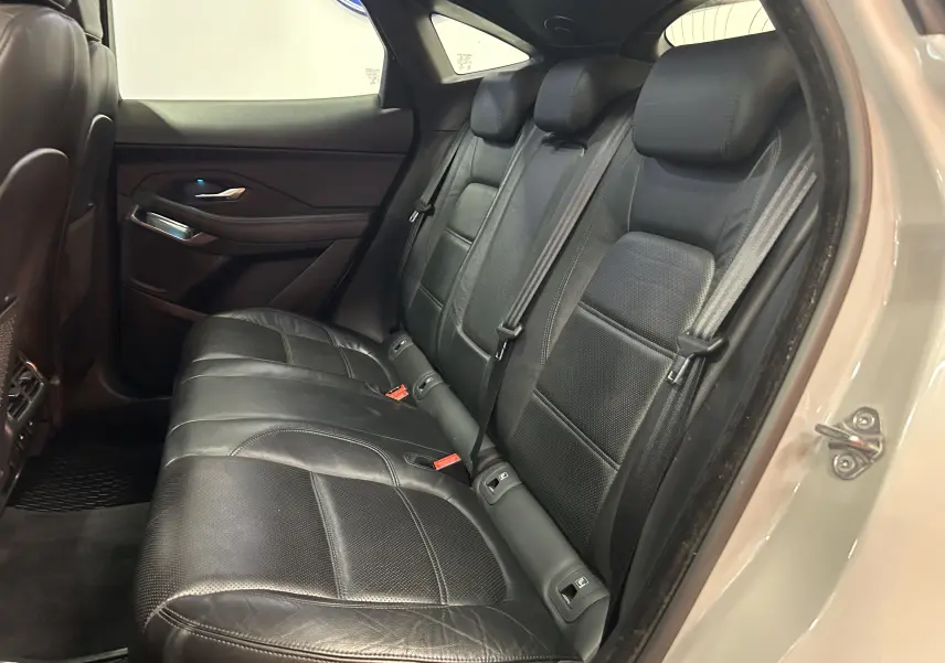 Vue intérieure des sièges arrière en cuir noir du Jaguar E-PACE beige, avec ceinture de sécurité et porte arrière ouvert côté droit.