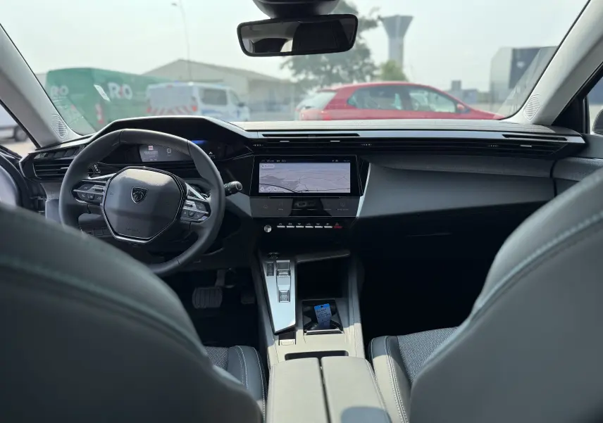 Intérieur moderne de la Peugeot 308 2025 en gris, vue depuis l'arrière montrant le volant compact et l'écran tactile central.
