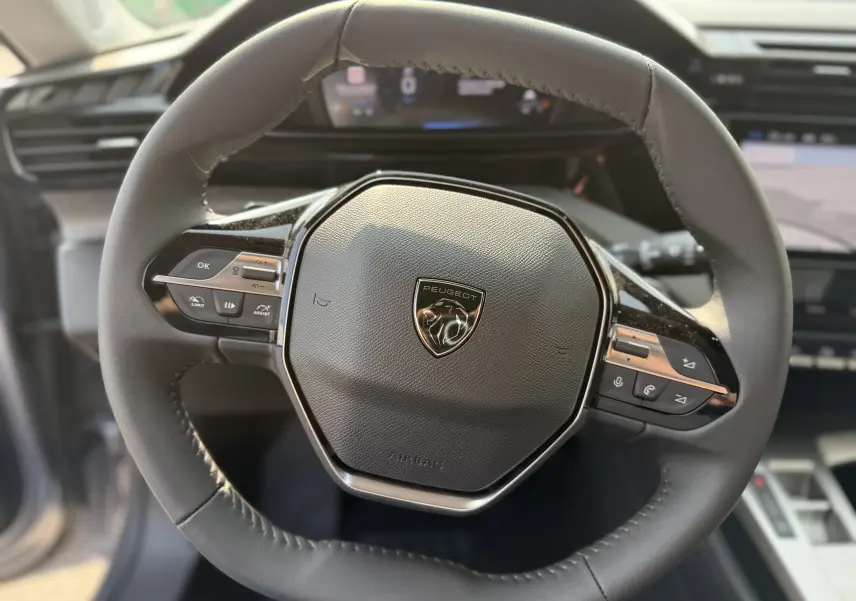 Gros plan sur le volant cuir noir du Peugeot 308 2025 avec commandes intégrées et logo lion au centre.