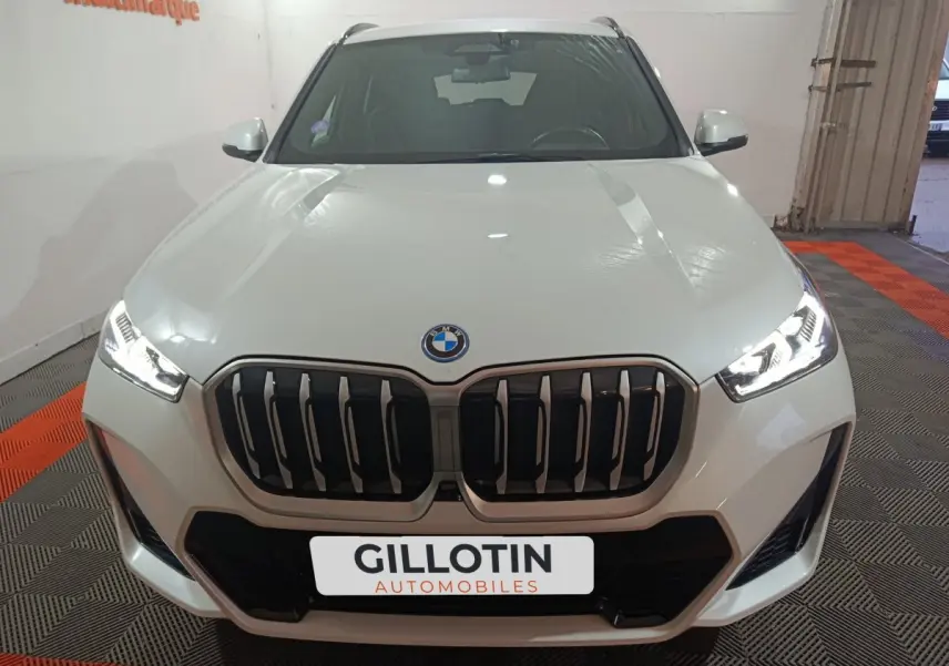 Vue frontale d’un BMW X1 blanc 2024 avec calandre imposante et phares LED allumés dans un garage.