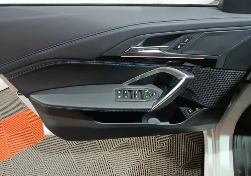 Vue intérieure côté gauche de la porte avant d’un BMW X1 blanc, avec commandes de vitres et surpiqûres bleues.
