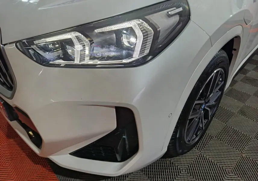 Gros plan sur l'avant droit blanc du BMW X1 xDrive25e M Sport 2024, mettant en valeur le phare LED et la jante noire.