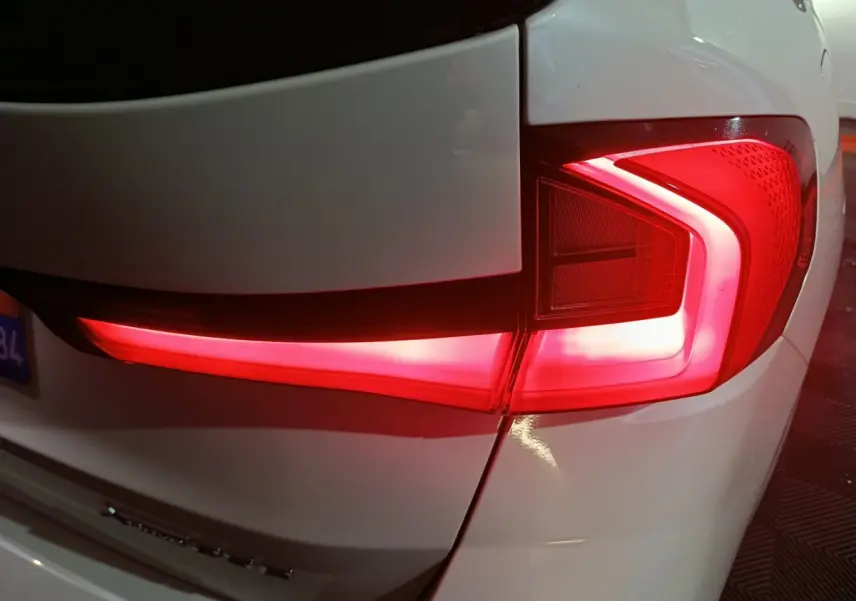 Gros plan sur le feu arrière droit rouge allumé d’un BMW X1 blanc, version xDrive25e M Sport 2024.