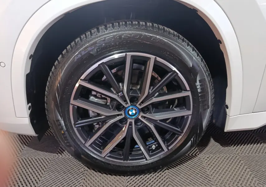 Gros plan sur la roue avant droite noire à jantes alliage du BMW X1 blanc xDrive25e M Sport 2024.