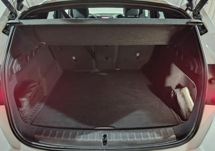 Coffre ouvert vu de l'arrière d'un BMW X1 blanc 2024, avec cache-bagages et intérieur noir épuré.