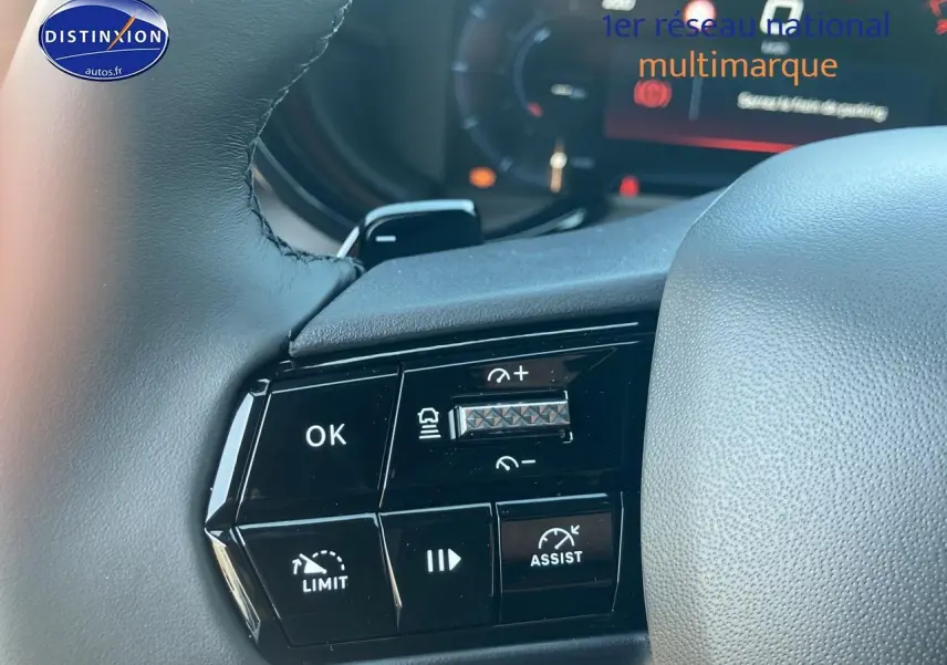 Gros plan sur les commandes à gauche du volant gris d'une Alfa Romeo Junior 1.2 hybride 2026, boutons noirs avec marquages blancs.