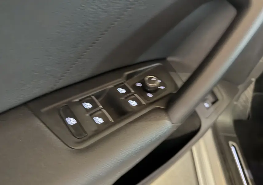 Gros plan sur les commandes des vitres électriques et réglages des rétroviseurs côté conducteur d’un Volkswagen Tiguan gris clair 2022.