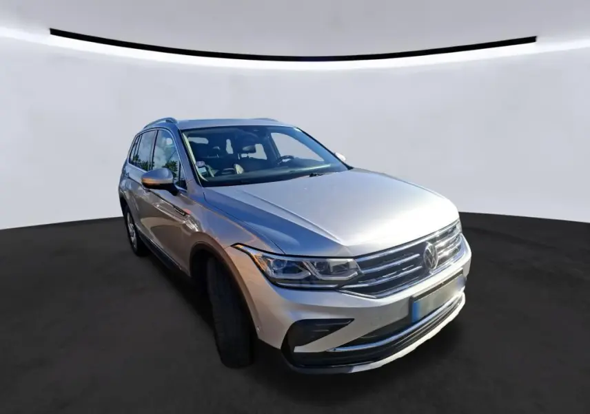 Volkswagen Tiguan gris clair en 3/4 avant droit, mettant en valeur sa calandre chromée et ses phares LED distinctifs.