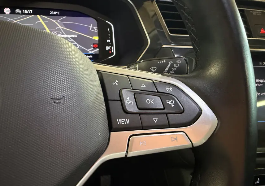Gros plan sur le volant noir du Volkswagen Tiguan 1.4 E-HYBRID 2022, avec commandes multifonctions et tableau de bord numérique en arrière-plan.