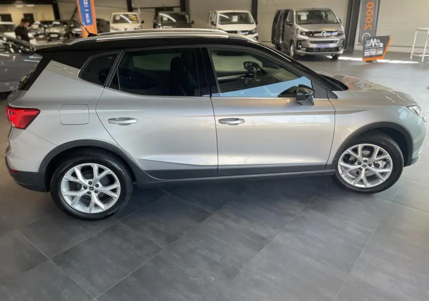 Vue de profil côté gauche d'un SEAT Arona 2024 gris clair avec toit noir et jantes alliage en showroom.