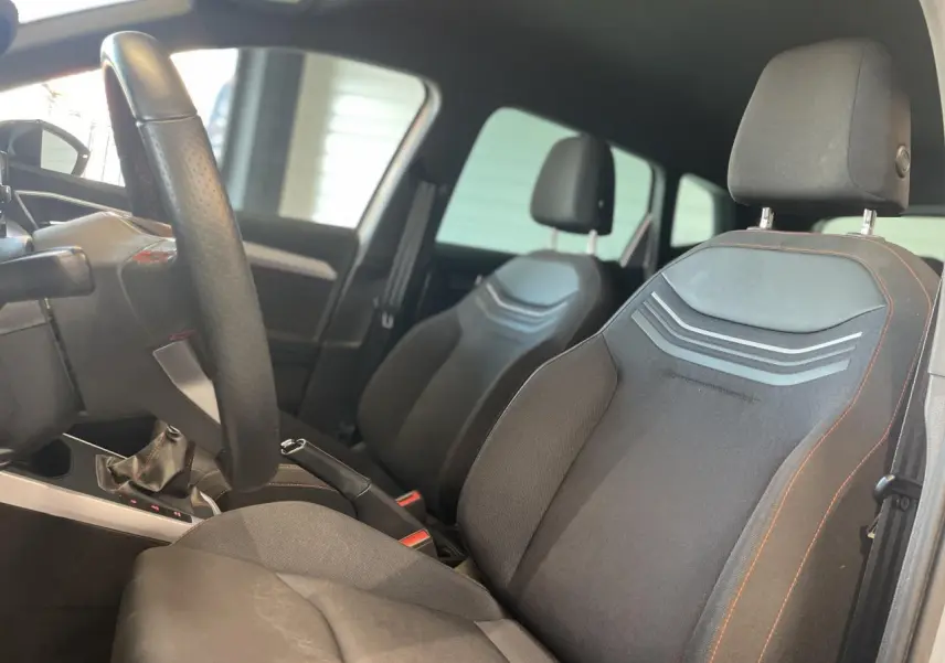 Vue intérieure côté conducteur du SEAT ARONA 2024 avec sièges textile noirs et volant sport cuir à méplat.