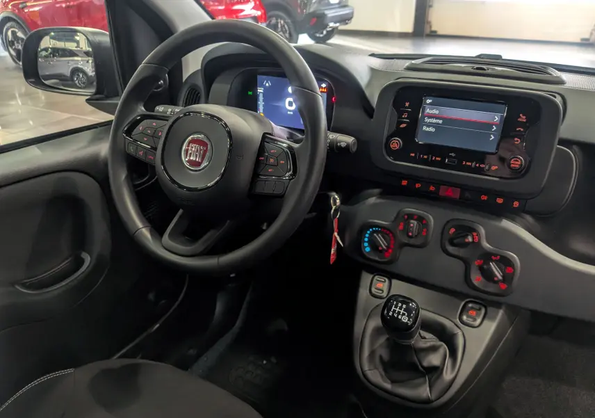 Vue intérieure côté conducteur de la Fiat Panda 1.0 Hybrid 2025 avec tableau de bord noir et commandes manuelles.