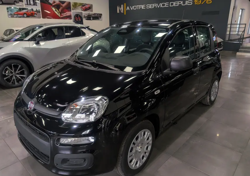 Vue 3/4 avant droite d'une FIAT Panda 1.0 Hybrid noire exposée en showroom avec ses phares et jantes visibles.