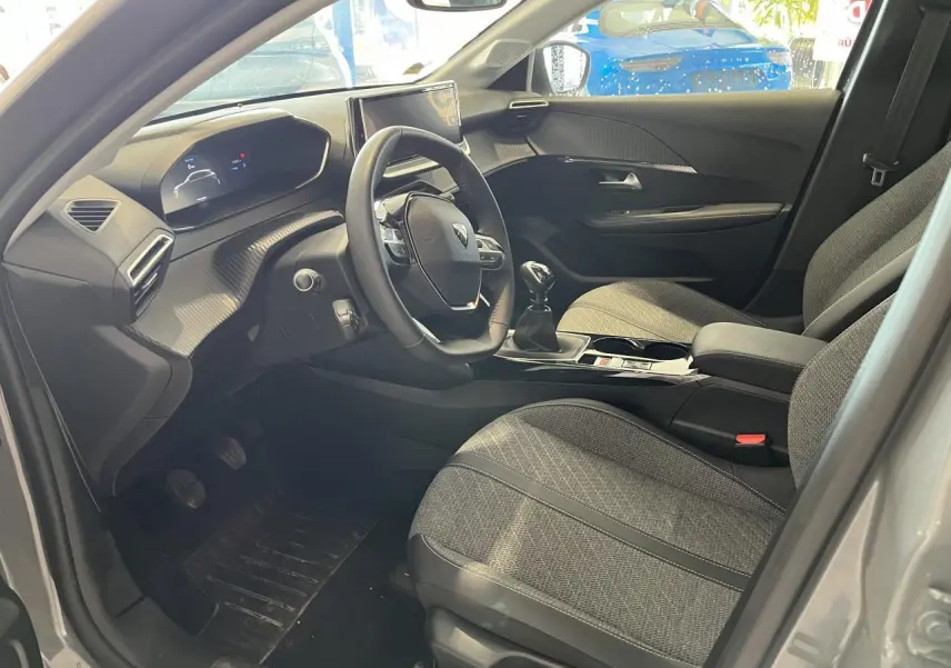 Intérieur avant droit du Peugeot 208 gris clair, volant compact cuir et sellerie tissu gris avec surpiqûres Quartz.