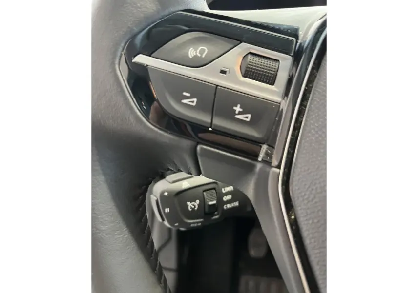 Gros plan sur les commandes multifonctions et régulateur de vitesse au volant cuir noir de la Peugeot 208 gris clair.