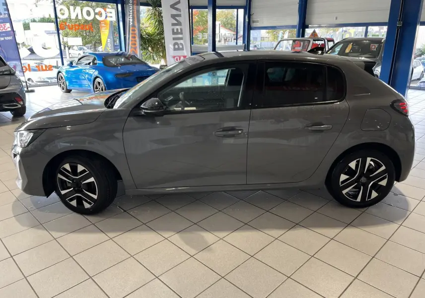 Profil droit d'une Peugeot 208 1.2 essence gris clair Selenium avec jantes alliage bi-tons, en intérieur showroom.