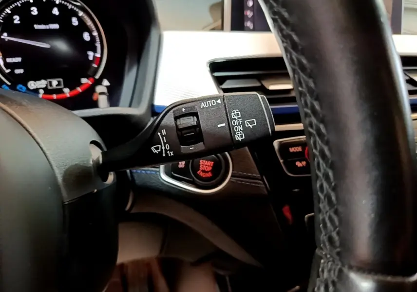 Gros plan sur la manette de commande d’essuie-glace à gauche du volant cuir noir dans l’habitacle du BMW X1 blanc 2022.