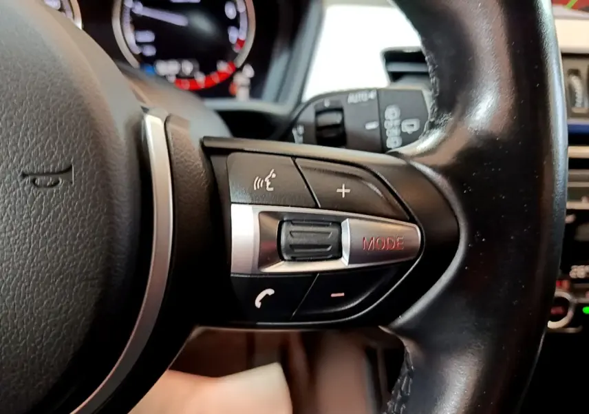 Gros plan sur la partie droite du volant noir en cuir du BMW X1 blanc, avec commandes audio et mode visibles.