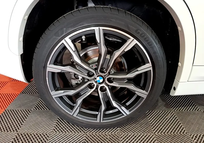 Gros plan sur la roue avant droite d’un BMW X1 blanc, jante alliage noire et argentée au design sportif.