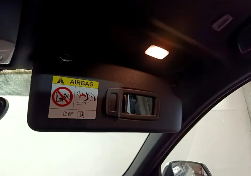 Vue intérieure rapprochée du pare-soleil côté conducteur avec miroir et avertissement airbag dans un BMW X1 blanc.