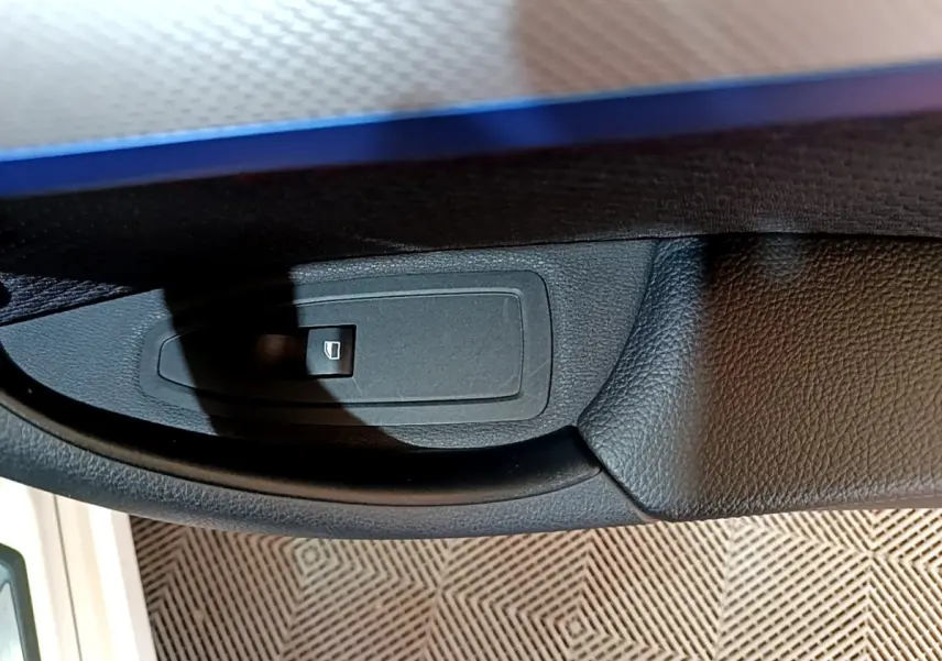 Gros plan sur le bouton de commande de lève-vitre côté conducteur d’un BMW X1 blanc, intérieur noir.