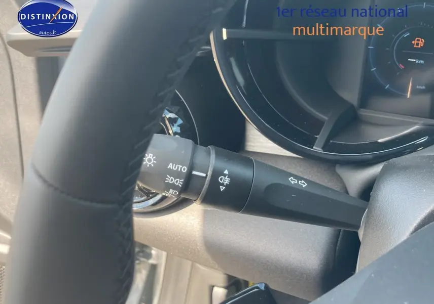 Gros plan sur la manette de clignotants et phares à gauche du volant d'une Alfa Romeo Junior grise, tableau de bord partiellement visible.