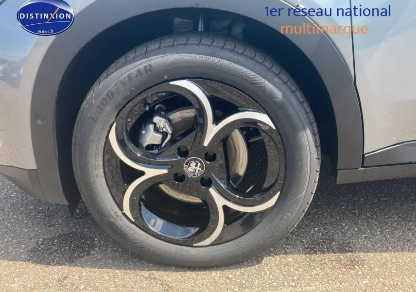 Gros plan sur la roue arrière gauche grise d'une Alfa Romeo Junior 1.2 hybride avec jante alliage noire et argent.