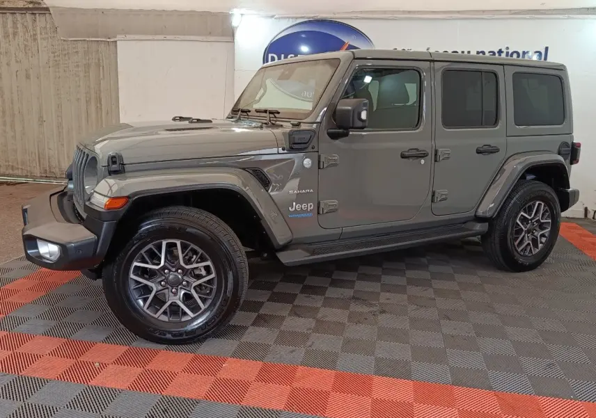 Jeep Wrangler Sahara gris foncé vu de profil côté gauche, avec jantes alliage et toit fermé.