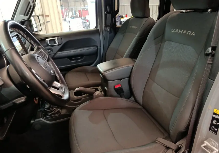 Vue intérieure côté conducteur de la Jeep Wrangler Sahara 2022 avec sièges noirs brodés "Sahara" et volant cuir.