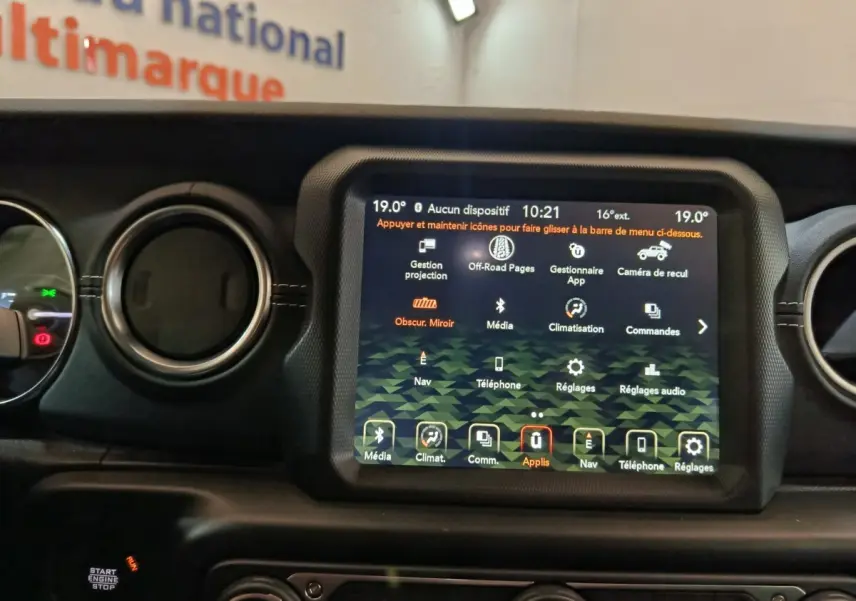 Écran tactile central allumé du tableau de bord d’un Jeep Wrangler gris foncé, avec commandes climatisation et multimédia visibles.