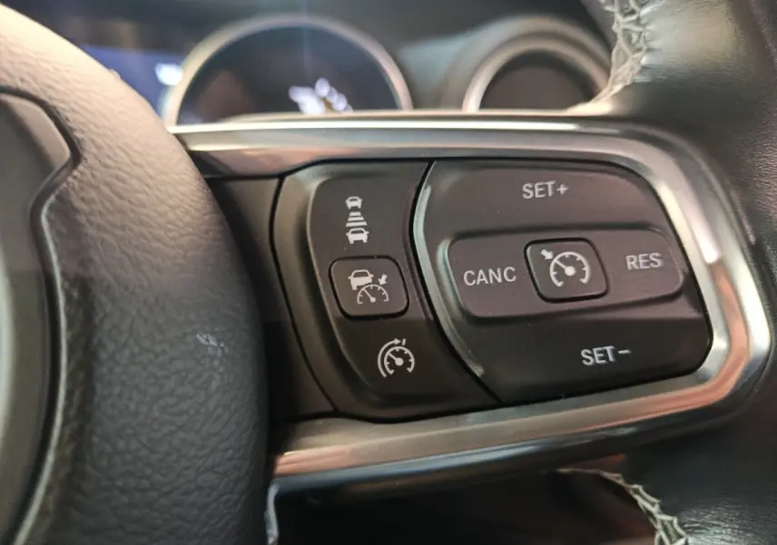 Gros plan sur les commandes du régulateur de vitesse au volant cuir noir de la Jeep Wrangler gris foncé 2022.