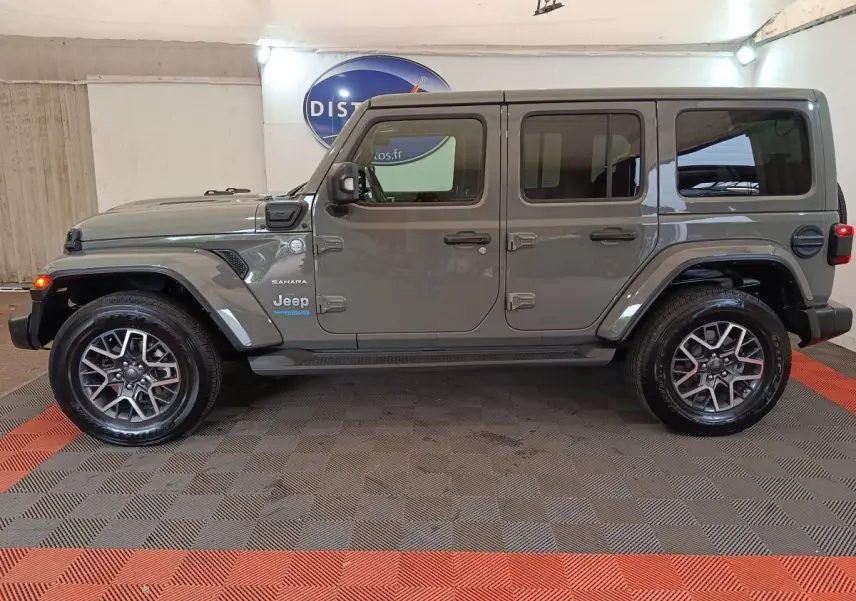 Vue de profil côté gauche d'un Jeep Wrangler Sahara gris foncé hybride rechargeable, avec jantes alliage et toit rigide.