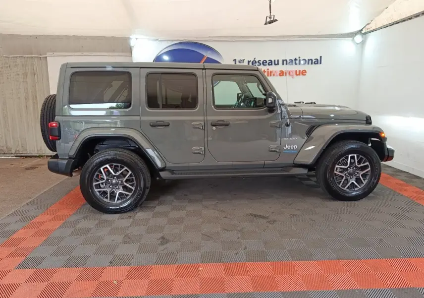 Jeep Wrangler Sahara gris foncé vue de profil côté gauche, avec roue de secours et jantes alliage visibles.