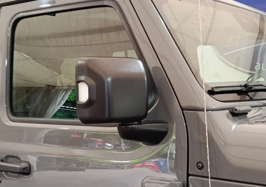 Vue latérale gauche rapprochée d’un Jeep Wrangler gris foncé mettant en valeur la portière et le rétroviseur noir.