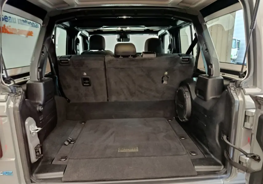 Vue arrière du coffre ouvert d’un Jeep Wrangler gris foncé 2022, montrant l’intérieur spacieux avec banquette arrière rabattue.