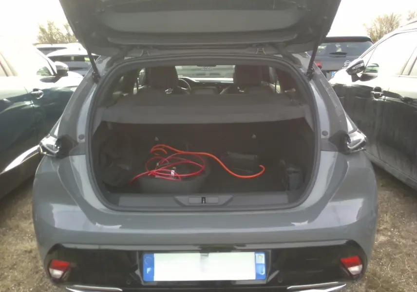 Vue arrière ouverte d'un Peugeot 308 gris clair 2024 avec coffre dévoilant un câble de recharge orange.