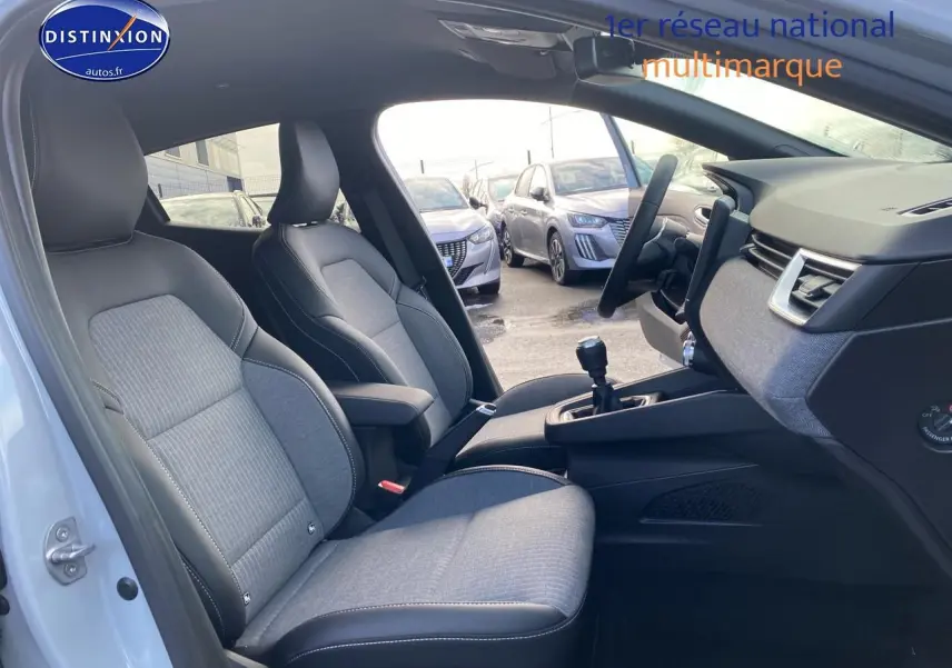 Vue intérieure côté conducteur de la Renault Clio V gris rafale, montrant les sièges tissu et la console centrale avec boîte manuelle.