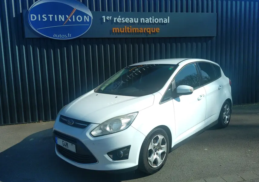 Ford C-MAX blanc vue 3/4 avant droit, garé devant un mur noir avec enseigne Distinxion.