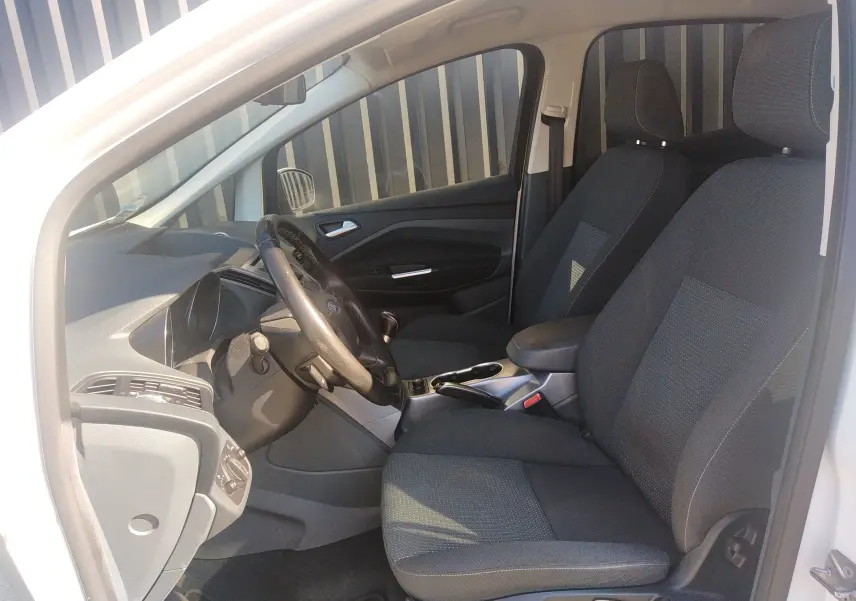 Vue intérieure côté conducteur du Ford C-MAX blanc de 2013, montrant les sièges en tissu noir et le tableau de bord.