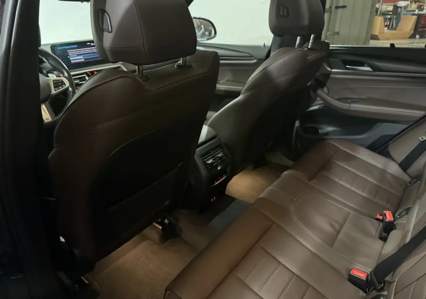Vue intérieure arrière droite du BMW X3 xDrive30e 2023 avec sièges en cuir marron et console centrale avec aérateurs.