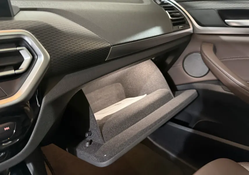 Intérieur BMW X3 xDrive30e 2023, vue côté passager sur boîte à gants ouverte et garnitures marron et noires.