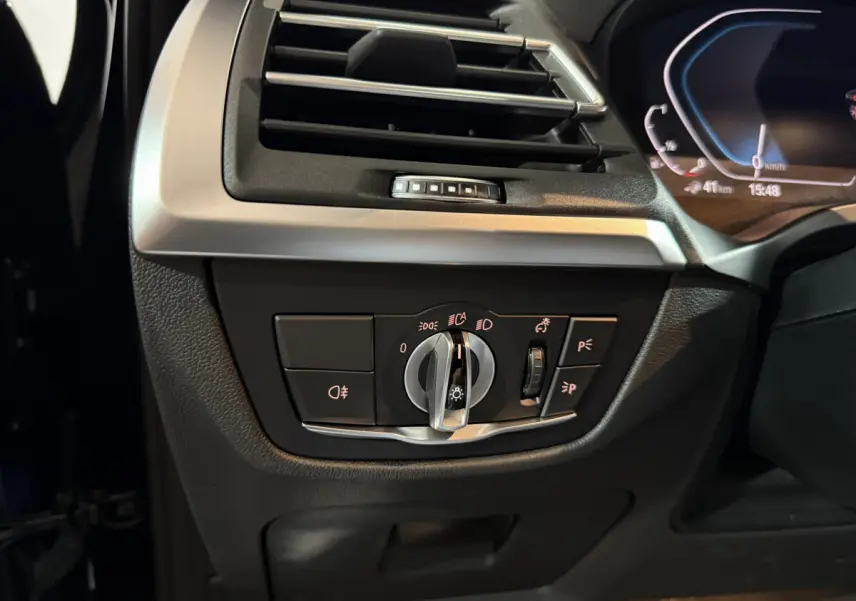 Détail du tableau de bord côté gauche du BMW X3 xDrive30e 2023, avec commande des phares et ventilation.