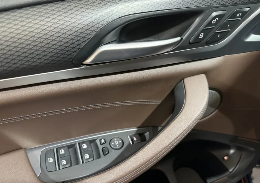 Gros plan sur la porte intérieure côté conducteur du BMW X3 xDrive30e 2023, avec garniture cuir marron et commandes électriques.