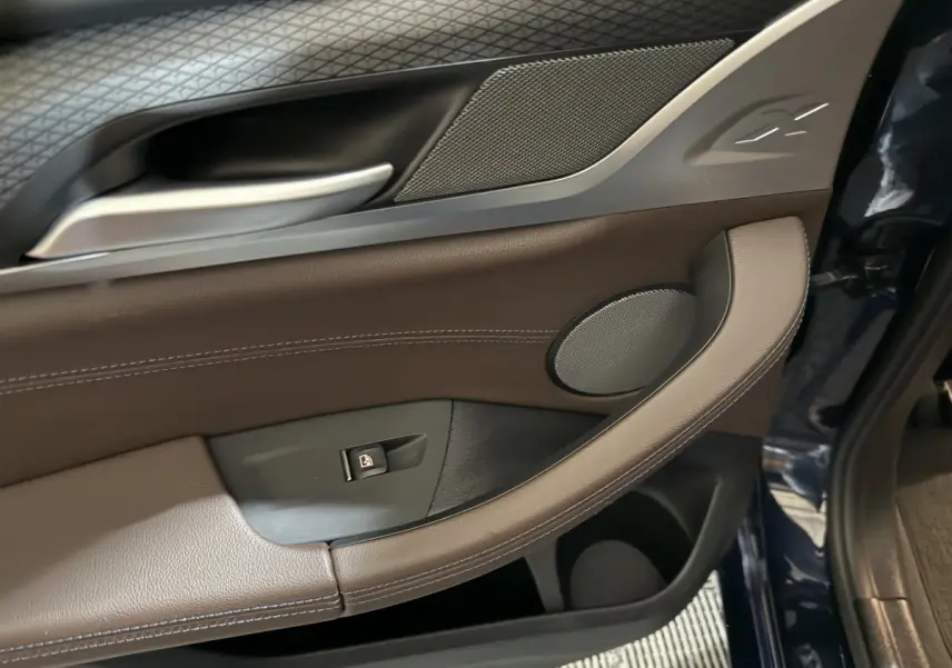Détail de la porte avant gauche du BMW X3 xDrive30e 2023 en bleu, avec garniture cuir marron et haut-parleur intégré.