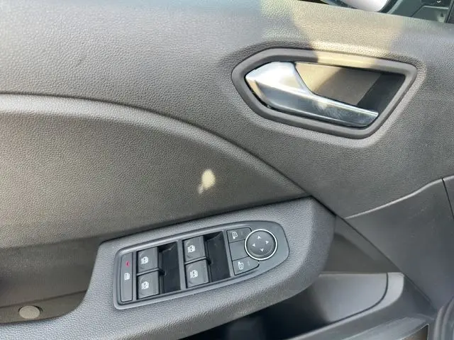 Gros plan sur la porte côté conducteur de la Renault Clio V blanche, montrant les commandes des vitres électriques et le bouton de réglage des rétroviseurs.