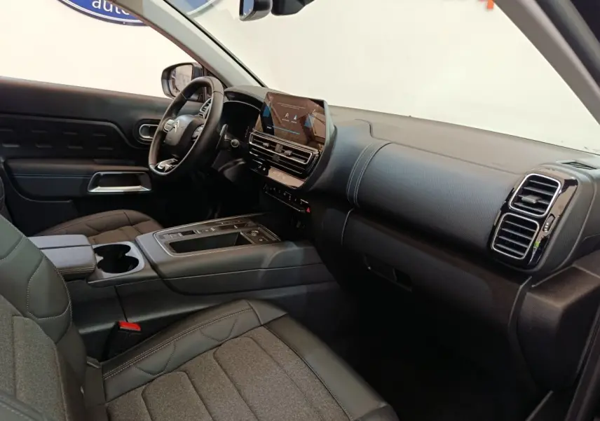 Vue intérieure côté conducteur du tableau de bord et console centrale du Citroën C5 Aircross 2024 noir avec écran tactile et volant cuir.
