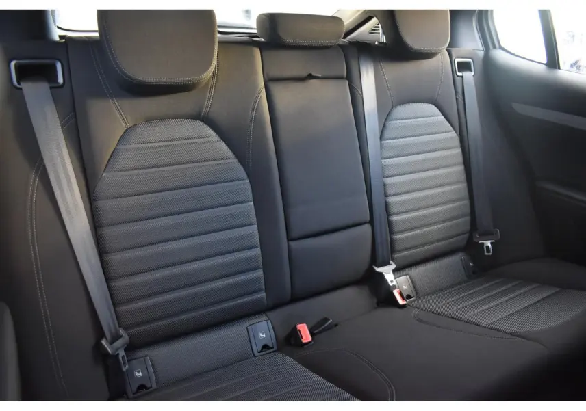 Vue intérieure sur les sièges arrière noirs en tissu et cuir de l'Alfa Romeo Stelvio 2024, avec ceintures de sécurité visibles.