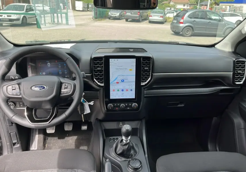 Vue intérieure avant du Ford Ranger 2025 gris carbone, avec tableau de bord moderne et écran tactile vertical central.